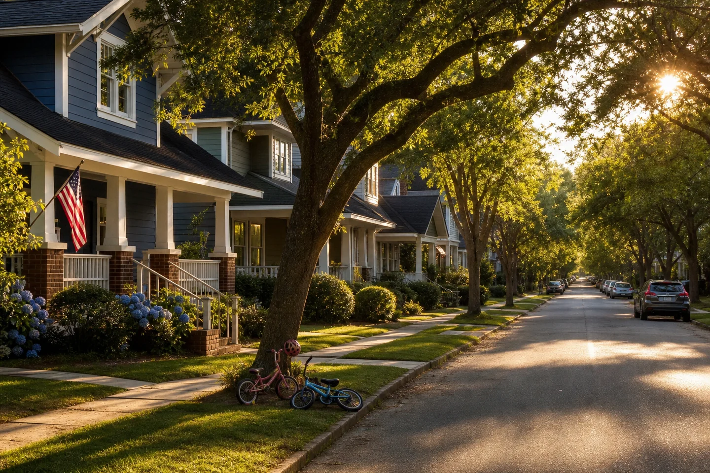 Quiet neighborhood street at sunset with craftsman front porches and children’s bikes under a shade tree